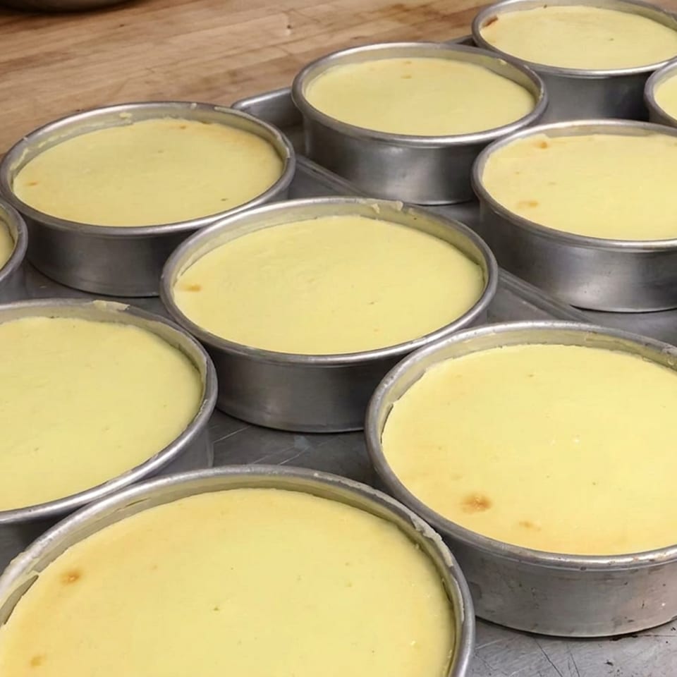 Tray of round metal pans filled with pale yellow custard desserts on a wooden worktable.