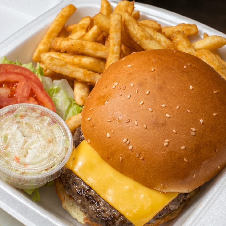 Cheeseburger with lettuce, tomato, fries, pickle spear, and coleslaw in a takeout container.