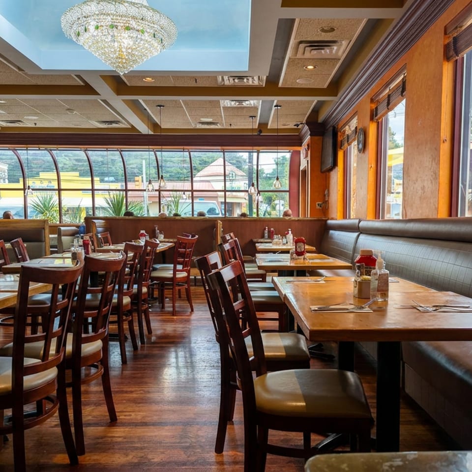 Warmly lit restaurant dining room with wooden tables, leather booths, large windows, and a crystal chandelier.